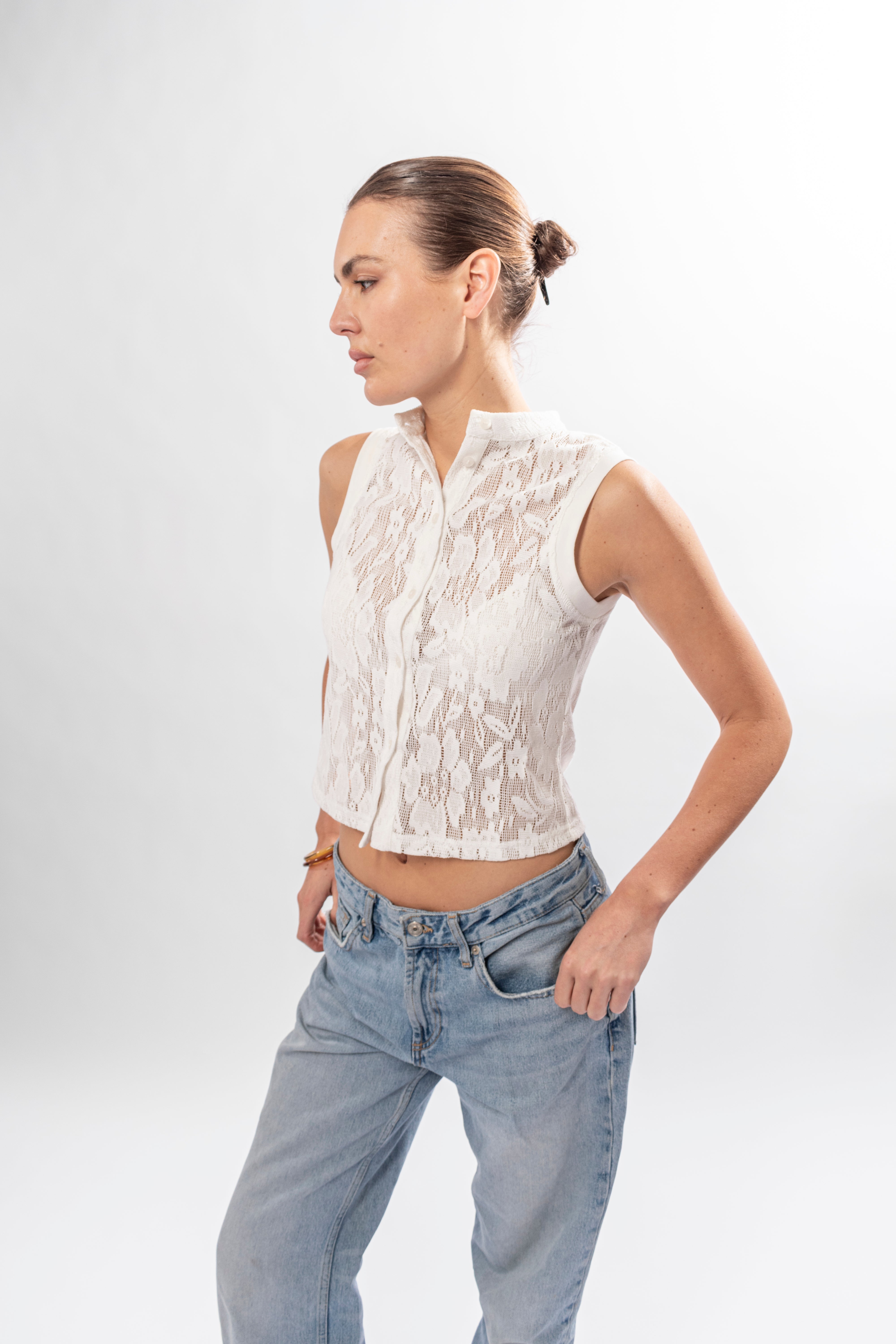 Woman wearing a white lace sleeveless top and blue jeans on a white background